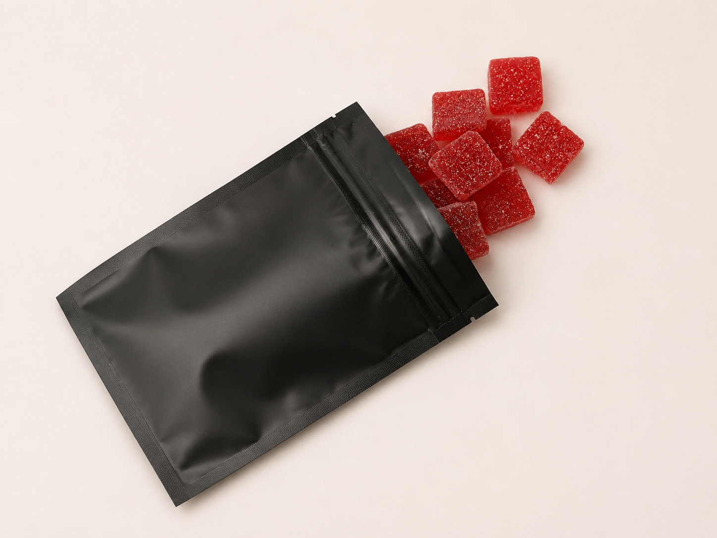 Red sugar-coated gummy squares spilling from a black pouch